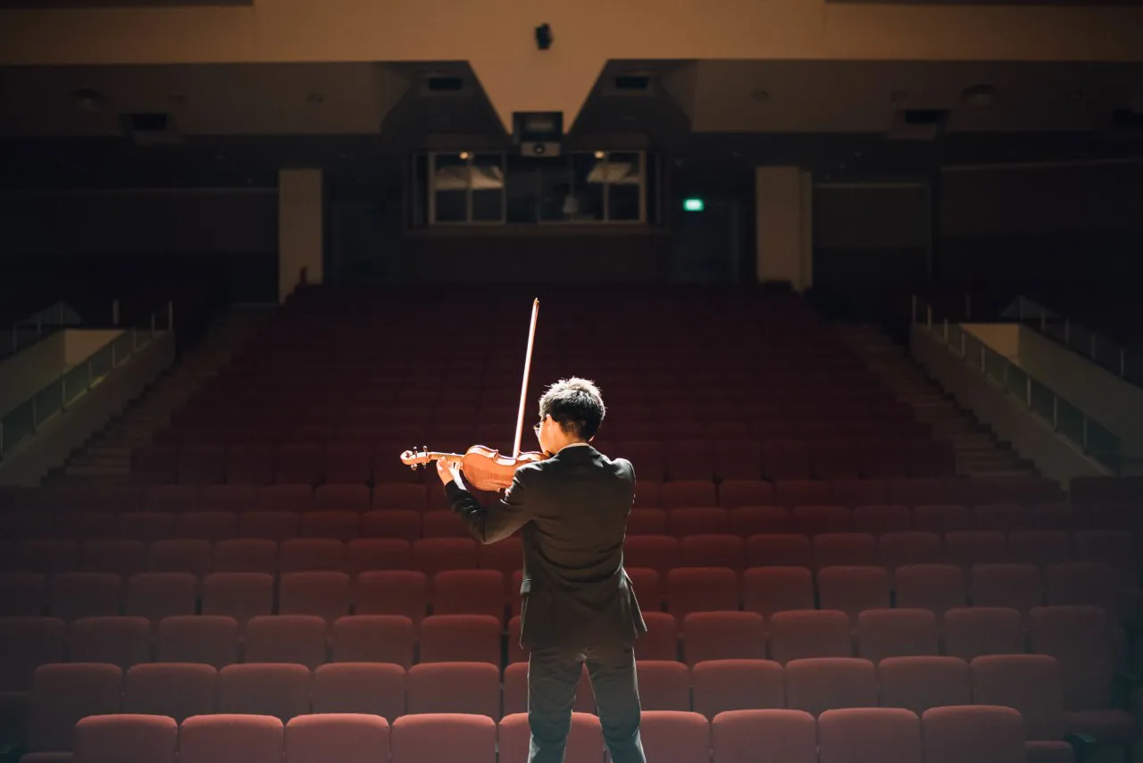 Adult violinist wearing a vest performing on stage