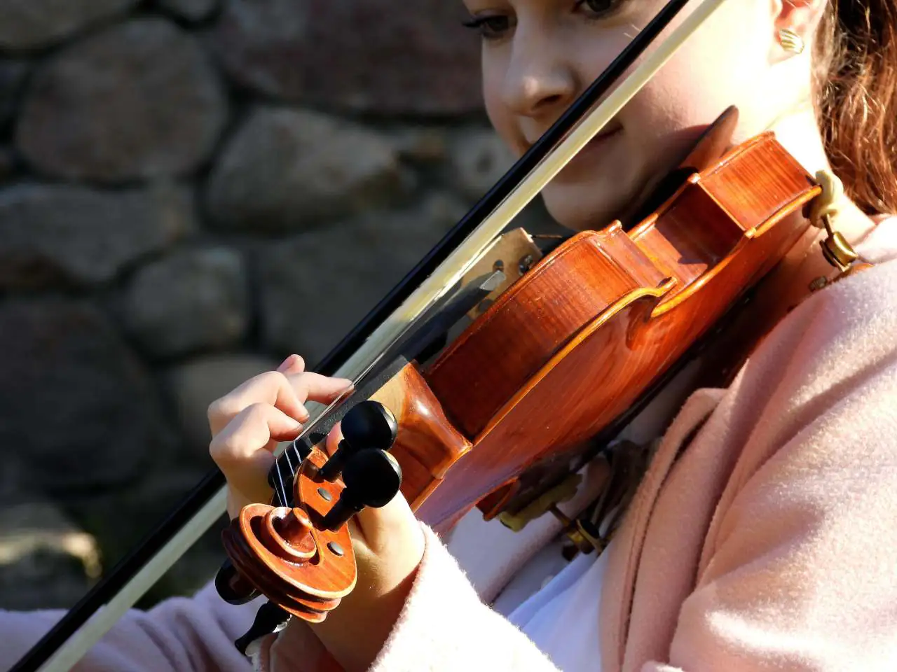 Girl wearing a pink coat while playing the violin.
