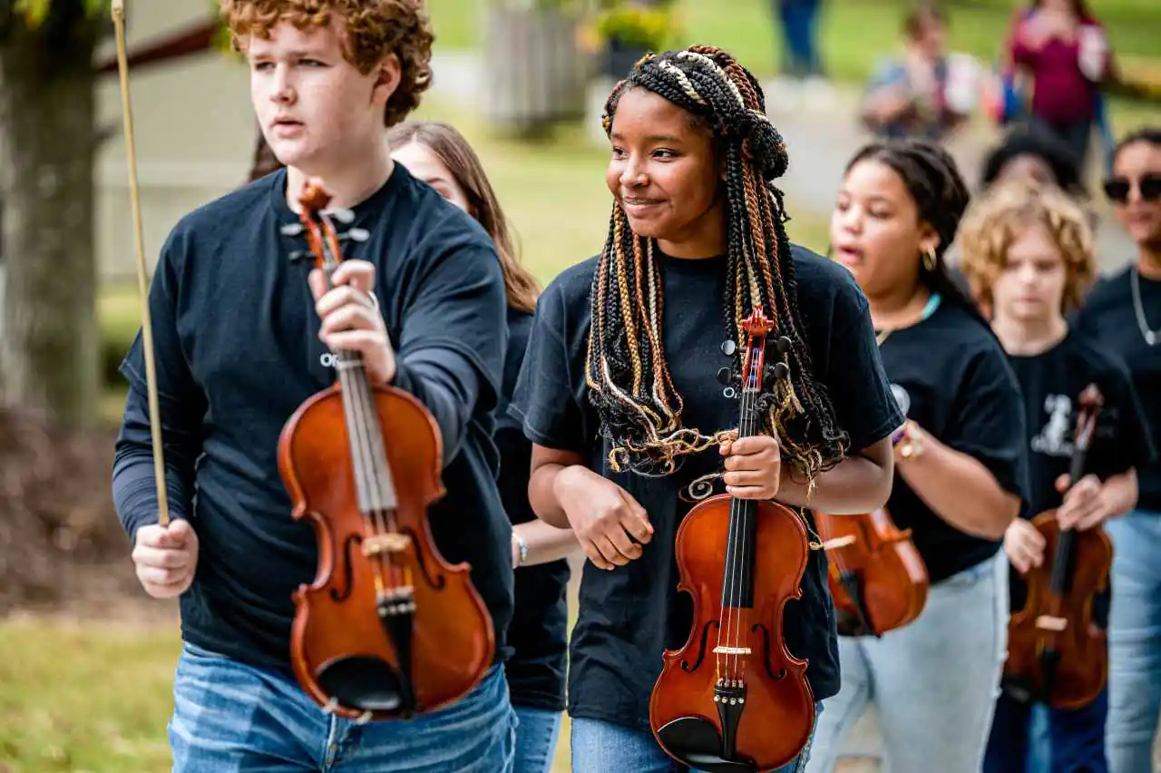 Teenage violinists walking outdoors with violins and bows