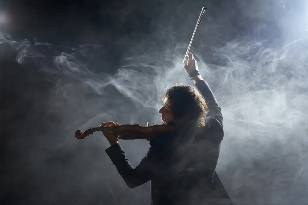 Violinist raising a violin bow through smoke before practicing fast violin techniques