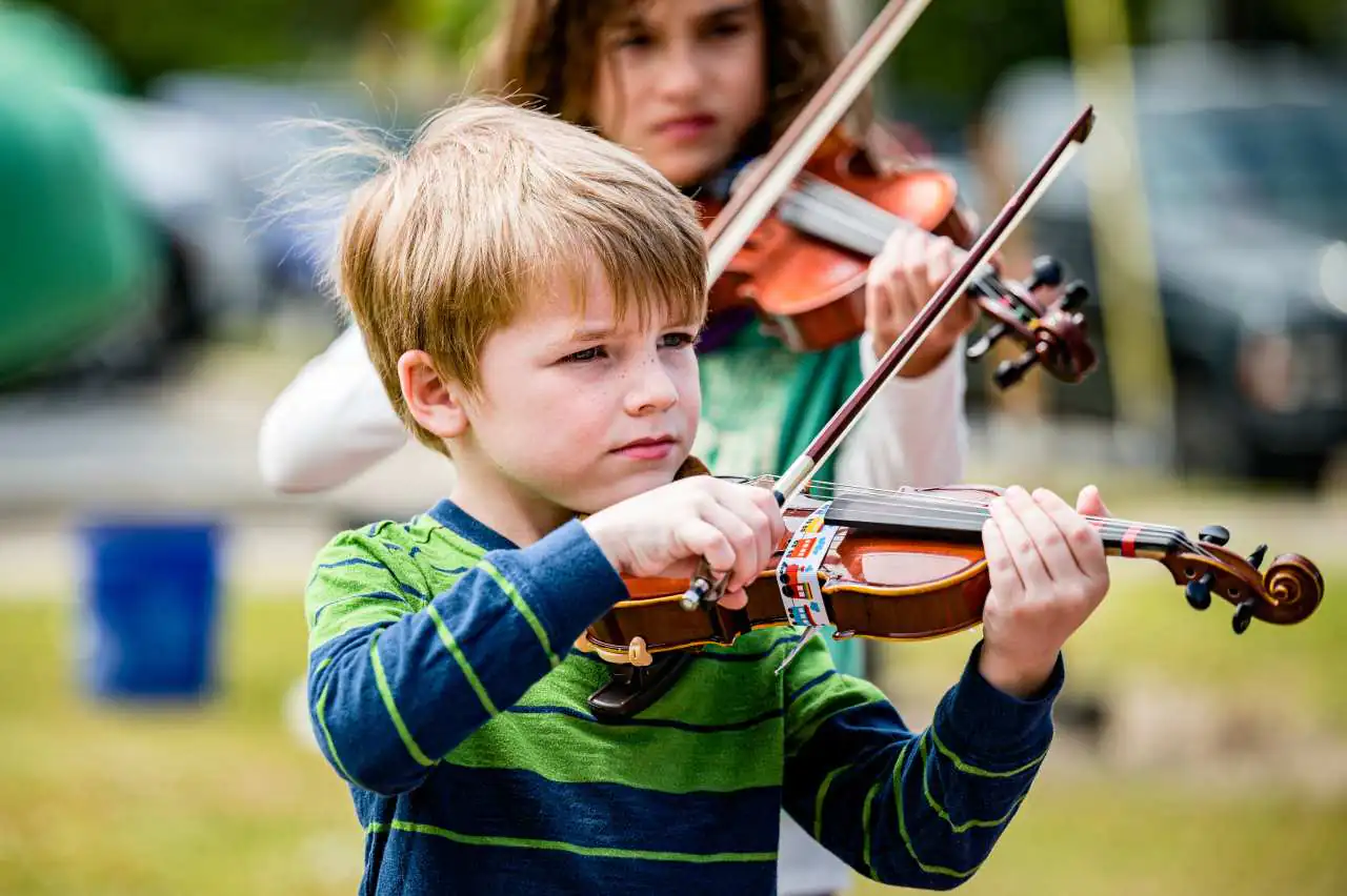 Young children playing violins outdoors